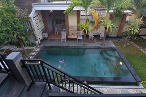 A swimming pool with a surrounding deck, a small patio area with chairs, and a staircase leading to an upper level. - Ons Canggu (Tibubeneng)