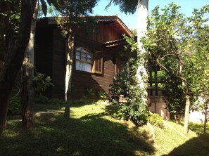 A rustic wooden cabin with a window and a door, surrounded by lush greenery and trees. - Pousada Villabella Villaggio (Florianópolis)