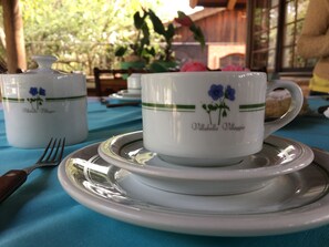 A table set with white ceramic cups and saucers featuring blue floral designs, placed on a blue tablecloth. - Pousada Villabella Villaggio (Florianópolis)