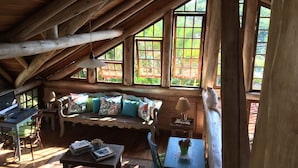 A cozy cabin with a wooden interior, a sofa with colorful cushions, a desk with a laptop, and large windows offering a view of greenery outside. - Pousada Villabella Villaggio (Florianópolis)