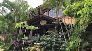 A rustic wooden building with a thatched roof, surrounded by lush tropical vegetation and flowering plants. - Pousada Villabella Villaggio (Florianópolis)