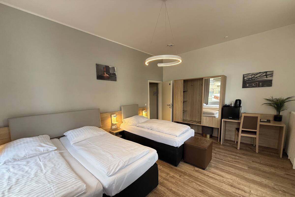 A modern hotel room with two beds, a desk, a chair, and a large mirror.