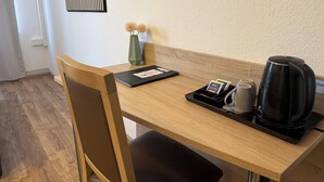 Un escritorio de madera con una computadora portátil, una bandeja con dos tazas, una cafetera y un florero con flores.