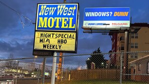 Deux enseignes de motel faisant la publicité du « New West Motel » et de « Dunn Windows & Doors ».