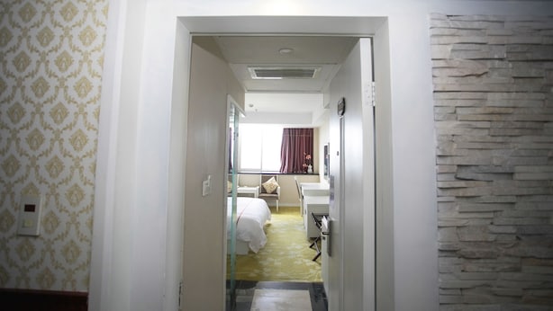 A hotel room with a bed, a desk, a chair, a mirror, and a stone wall. - Jiaxing ShiMao Inn (Jiaxing)