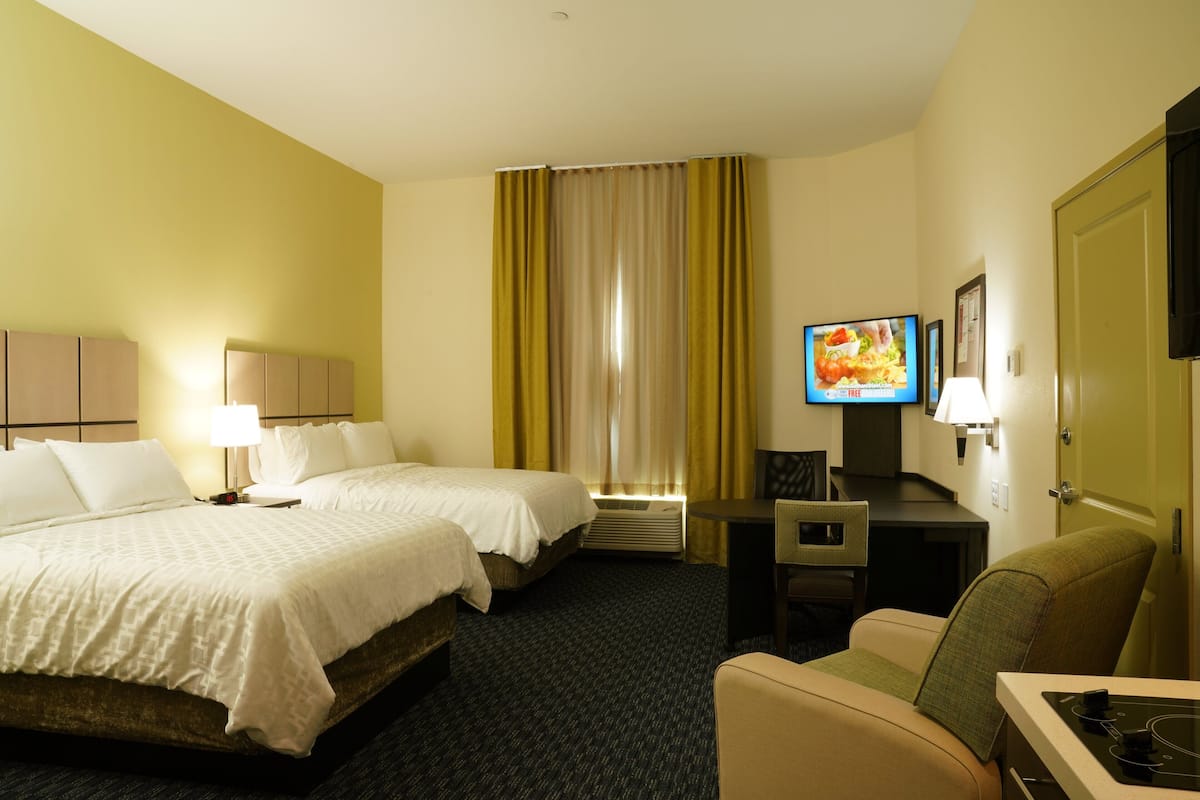 A hotel room with two beds, a desk, a chair, a television, and a door.