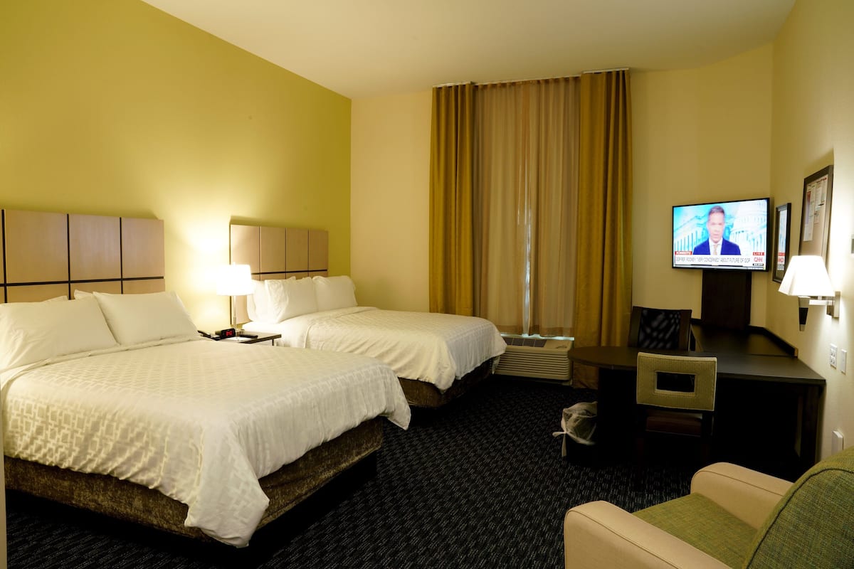 A hotel room with two beds, a desk, a chair, a television, and a window with curtains.