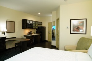 A hotel room with a bed, a desk, a chair, a kitchenette, and a framed picture on the wall. - Candlewood Suites Plano North by IHG (Plano)