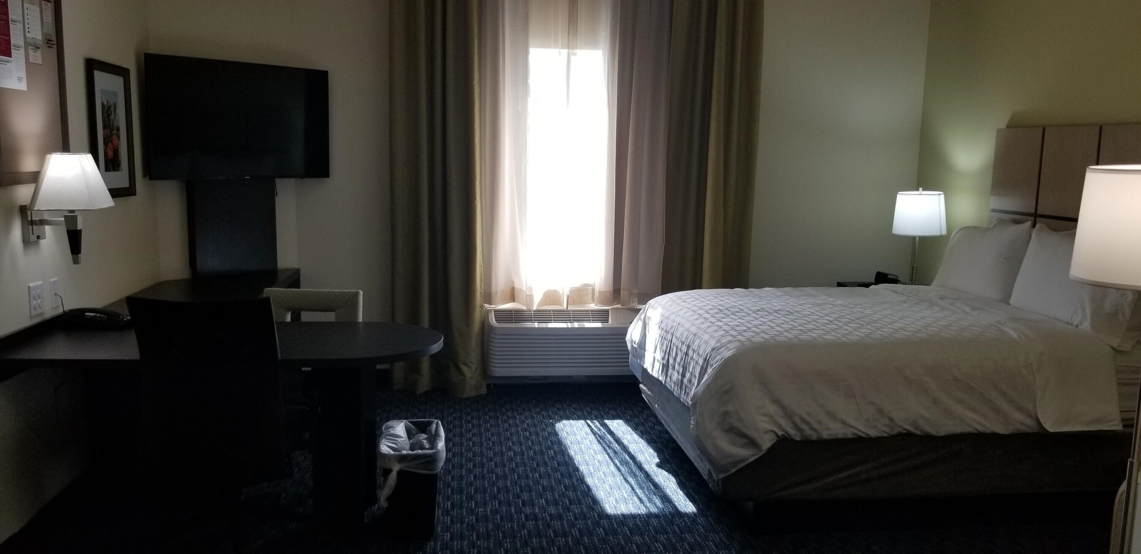 A hotel room with a bed, a desk, a chair, a TV, and a window with curtains.
