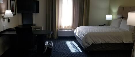 A hotel room with a bed, a desk, a chair, a TV, and a window with curtains.