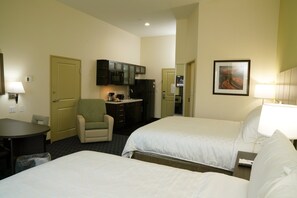 Two single beds with white linens, a desk, and kitchenette area with microwave, refrigerator, and coffee maker.
