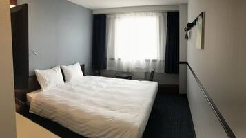 Una habitación de hotel con una cama grande, un escritorio pequeño, una silla y una ventana con cortinas.