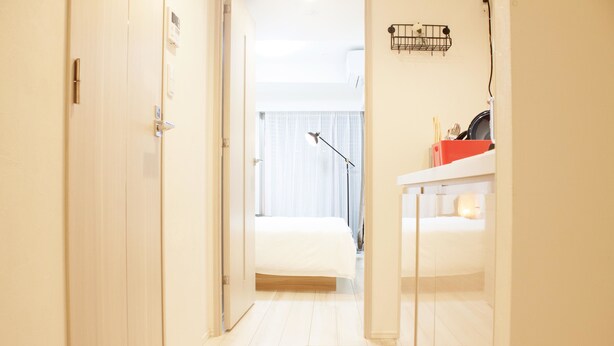 Un pasillo estrecho que conduce a un dormitorio con una cama, una mesita de noche y una lámpara.