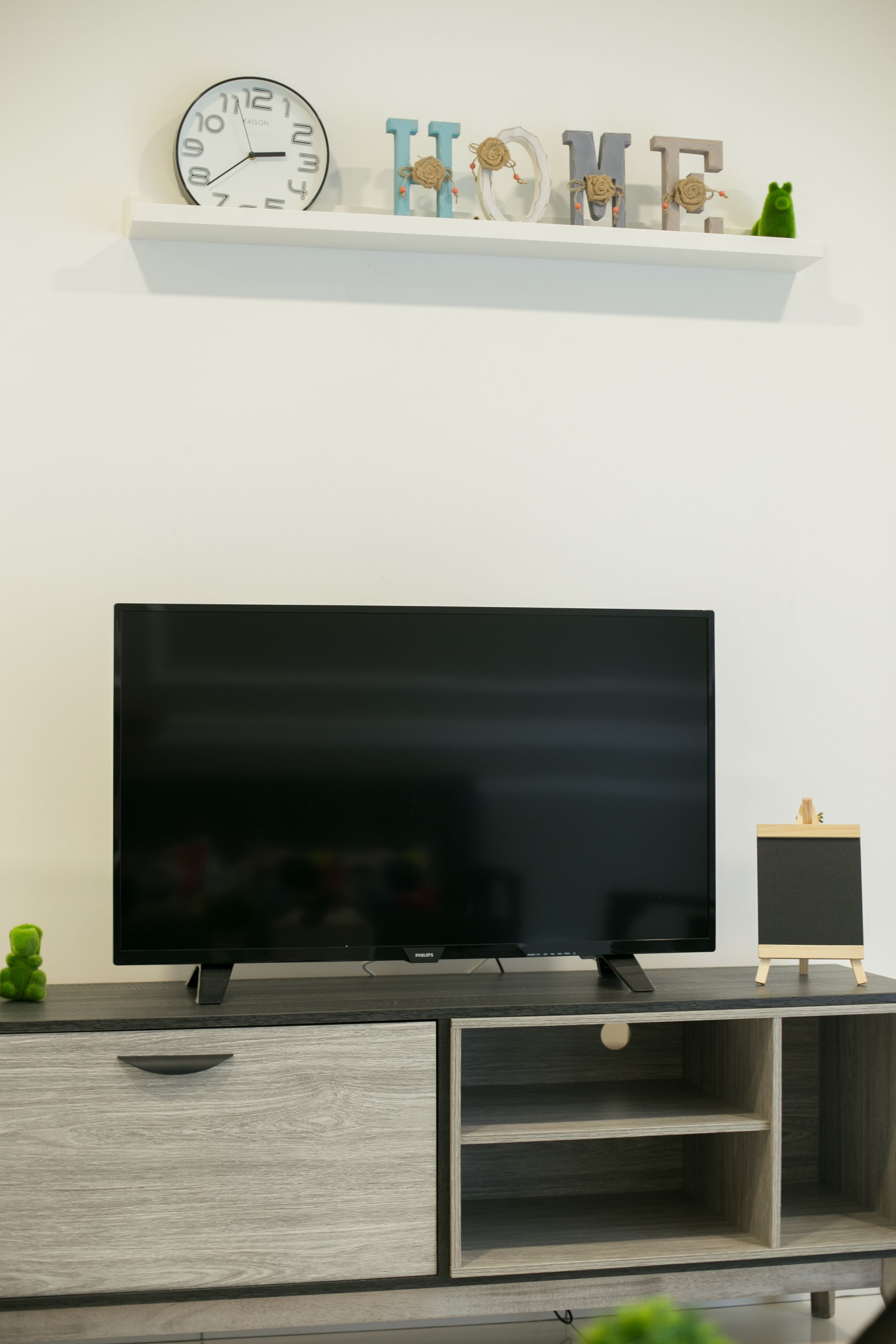Ein Flachbildfernseher auf einem Holz-TV-Schrank mit einem kleinen Holzregal darüber.