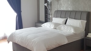 Ein modernes Schlafzimmer mit grauem Kopfteil, weißer Bettwäsche, einer Nachttischlampe und einem Deckenventilator.