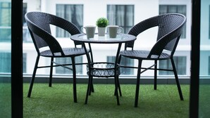Ein Balkon mit zwei Korbstühlen und einem kleinen Tisch, mit Blick auf ein modernes Gebäude mit vielen Fenstern.