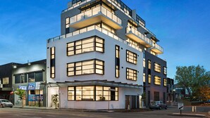Een modern meerhoog gebouw met grote ramen en balkons, gelegen op een hoek van een straat.