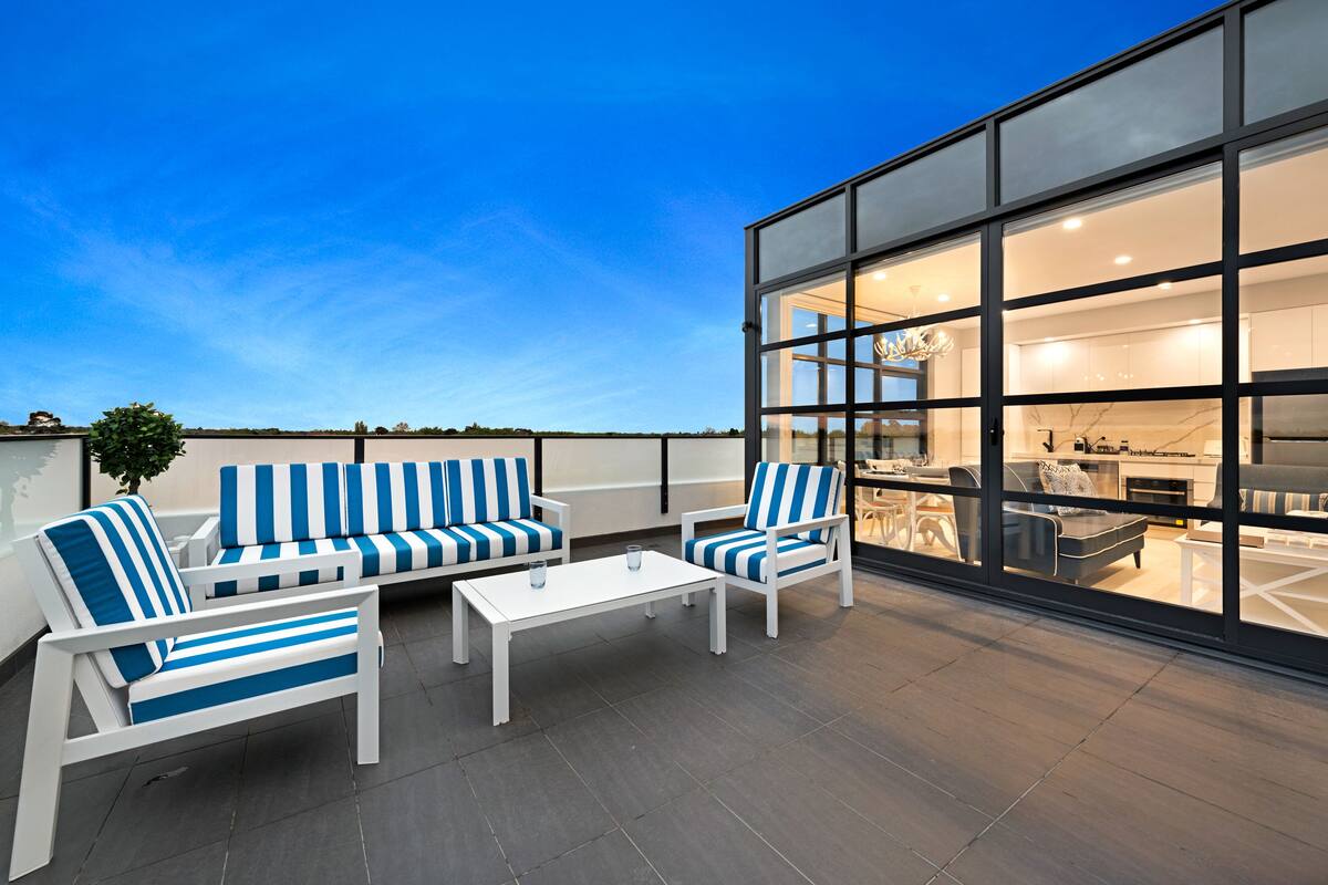 A rooftop terrace with a white sofa set, two armchairs, and a coffee table.