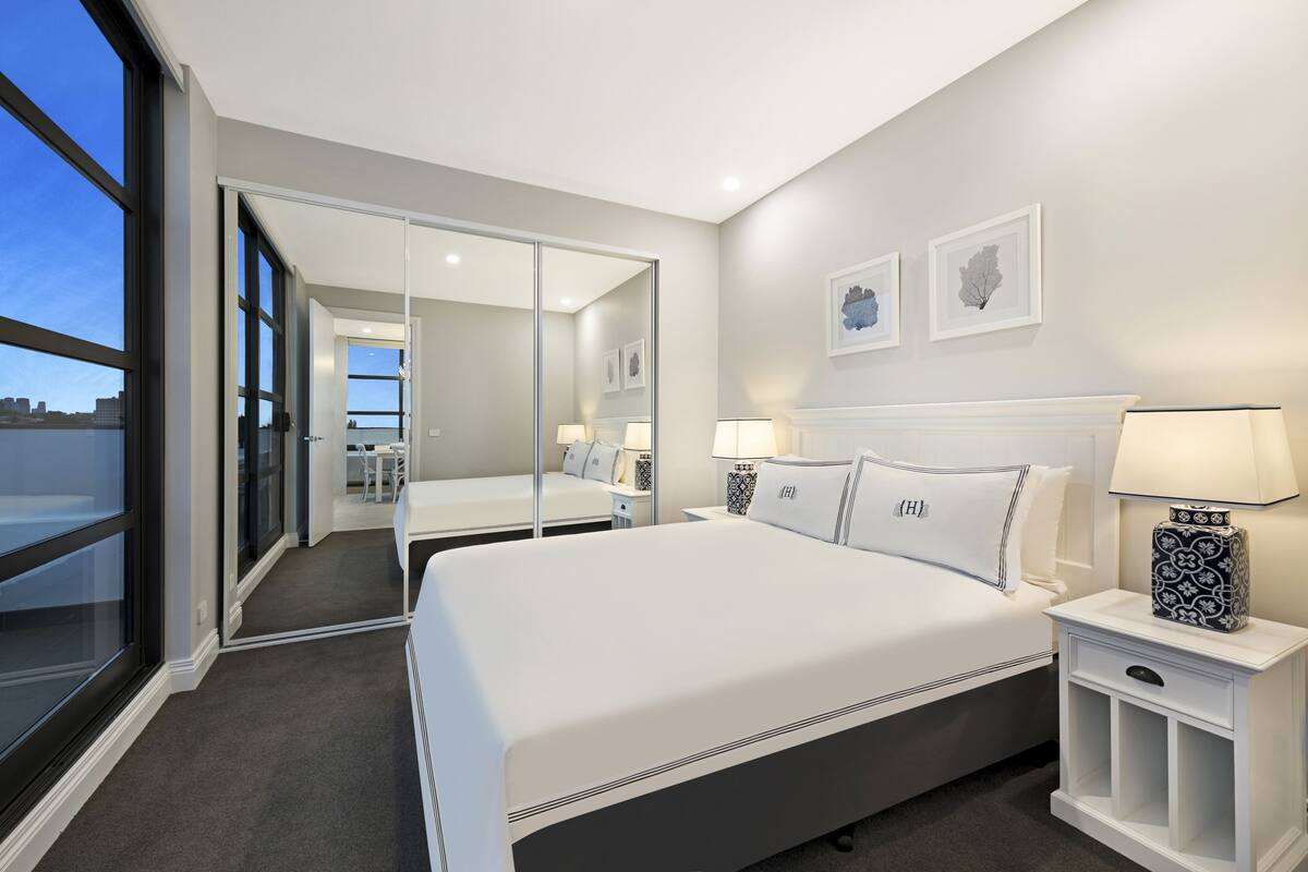A modern hotel room with a large bed, bedside tables, a mirror, and artwork on the wall.