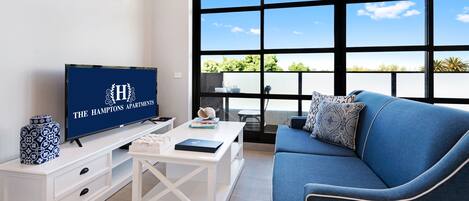 A modern living room with a large window, a flat-screen TV, a sofa, and a white coffee table.
