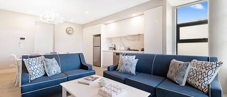 Een moderne woonkamer met twee blauwe banken, een witte salontafel en een eethoek met een witte tafel en stoelen.