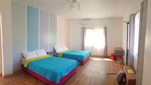 Ein Zimmer mit zwei Betten, Holzboden, Schreibtisch und einem Fenster mit Vorhängen.