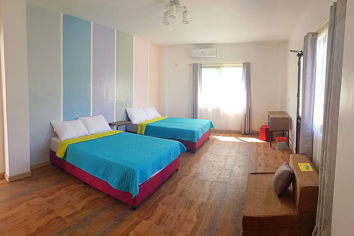 A room with two beds, a wooden floor, a desk, and a window with curtains.