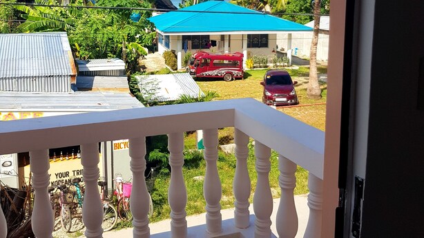 Ein Balkon mit Blick auf eine Wohngegend, darunter Häuser mit blauen Dächern, parkende Autos und Palmen.