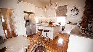 A modern kitchen with white cabinetry, a stainless steel refrigerator, and a large island with stools. - Belmont at Beechworth (Beechworth)