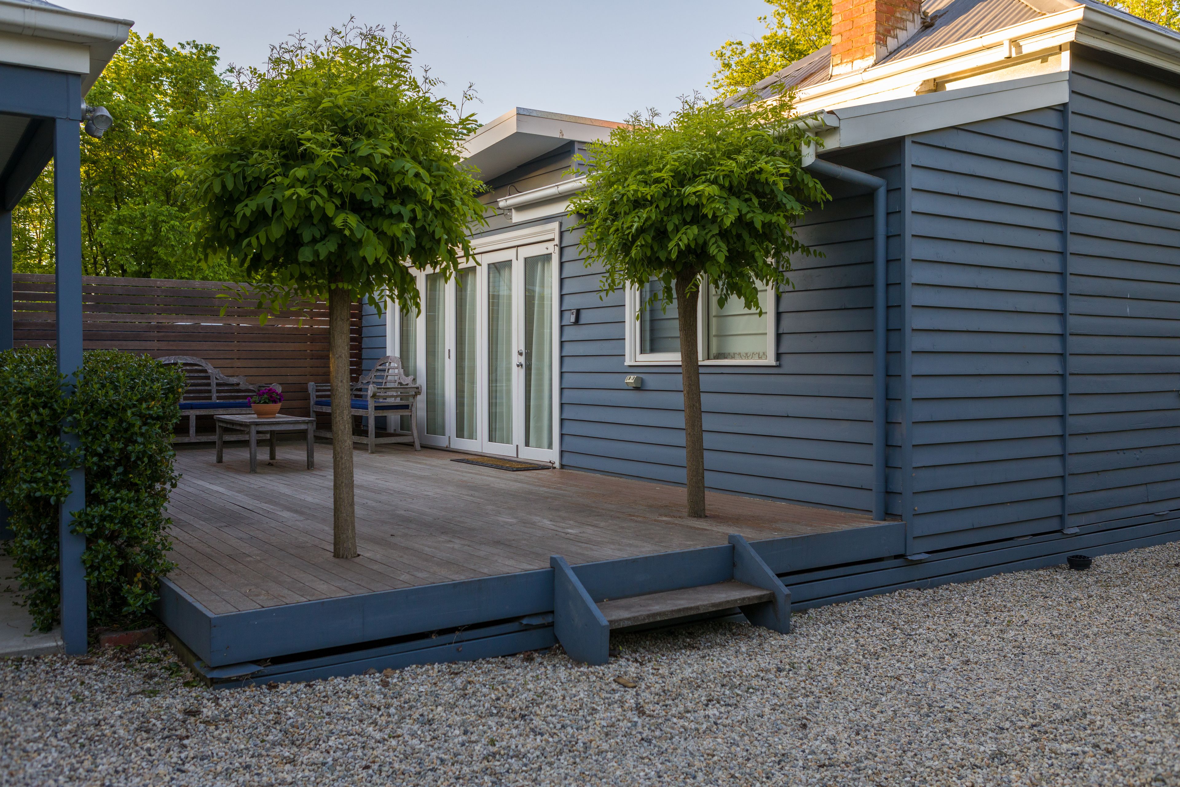 Un espacio al aire libre techado con una terraza de madera, dos árboles y un banco.