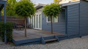 Un espacio al aire libre techado con una terraza de madera, dos árboles y un banco.
