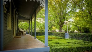 A porch with a covered seating area, a hedge, and a tree in the background. - Belmont at Beechworth (Beechworth)