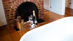 A room with a brick fireplace, a flat-screen TV mounted above it, a white bathtub, and a tray with champagne glasses and a bottle. - Belmont at Beechworth (Beechworth)