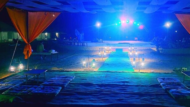 A beachside venue with a stage, seating area, and ambient lighting. - Desert Raasleela Camp (Jaisalmer)