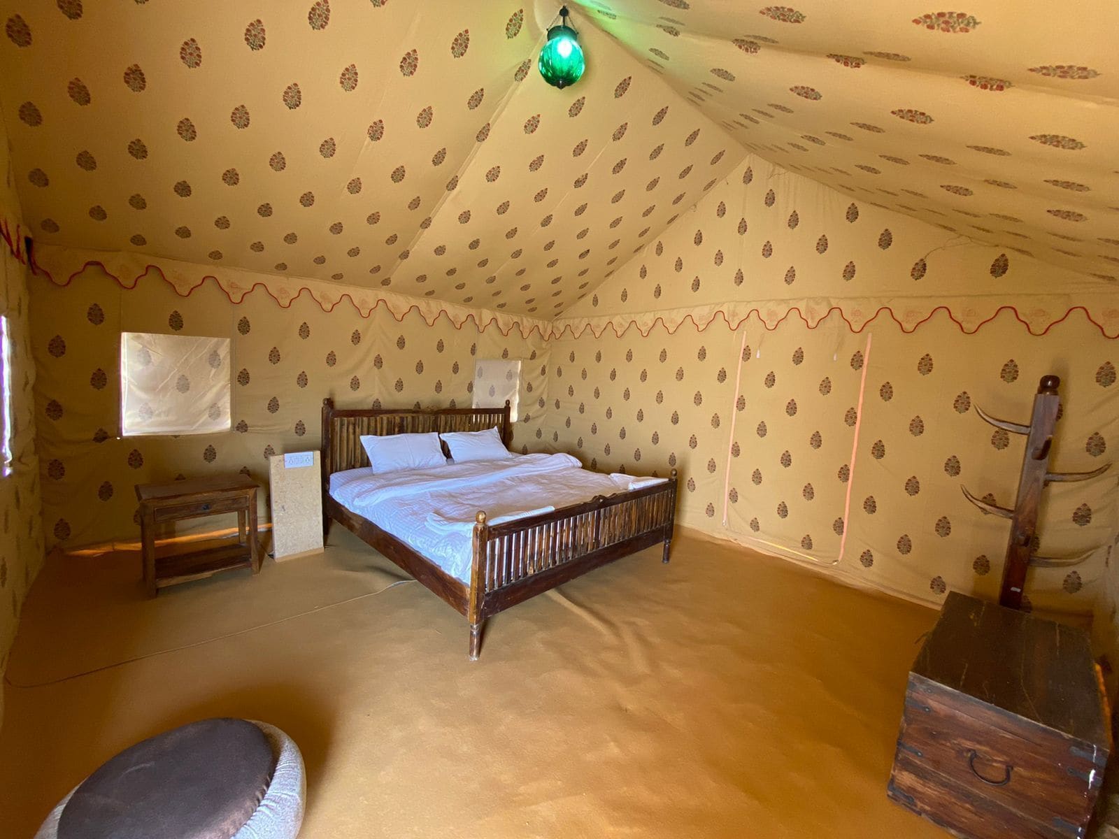 A bedroom with a bed, a small table, a chair, a wooden chest, and patterned walls.