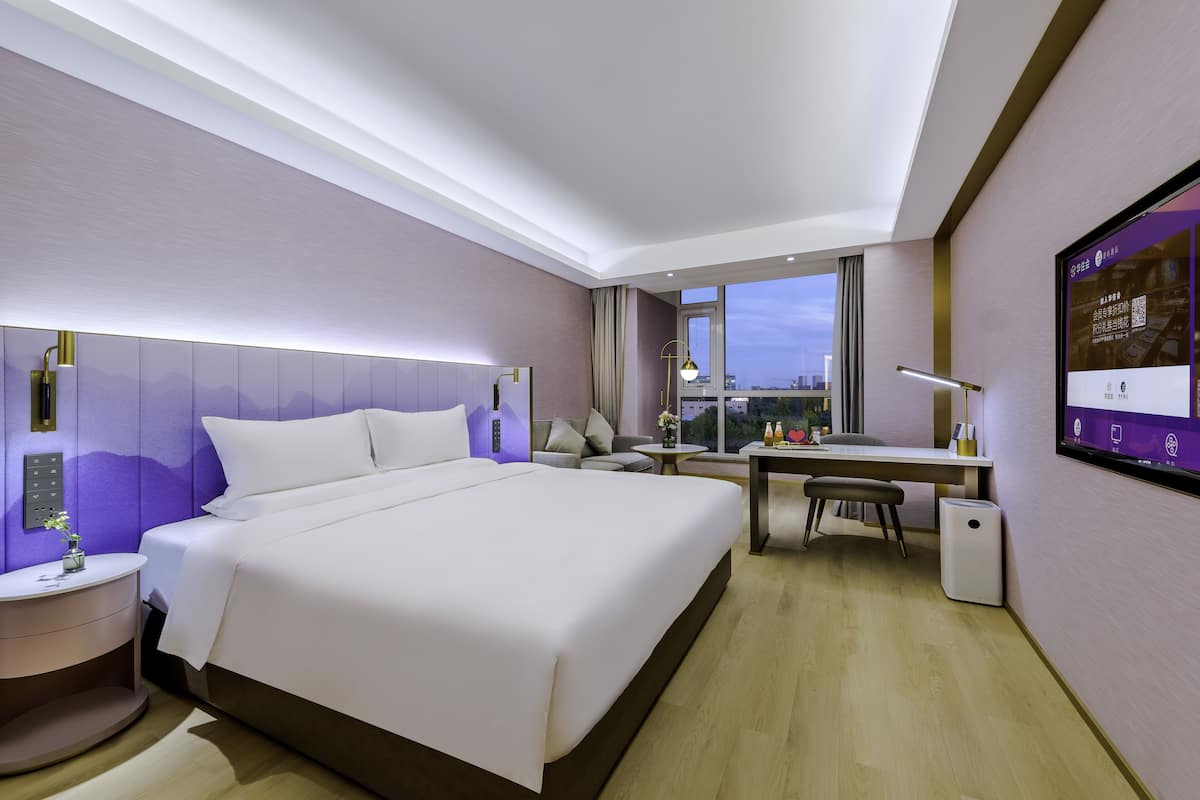 Ein modernes Hotelzimmer mit einem großen Bett, einem Schreibtisch und Blick auf die Stadt.