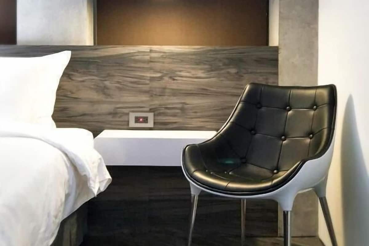A modern bedroom with a bed, a chair, a wall-mounted light, and a wooden accent wall.