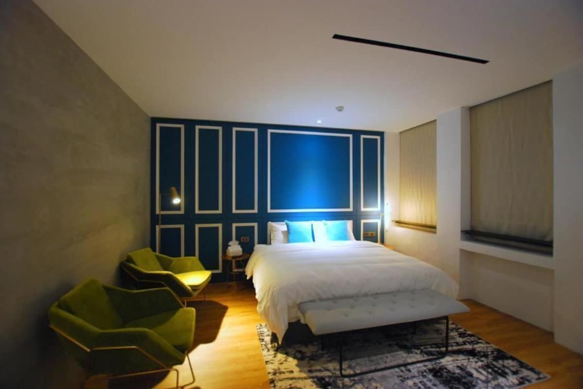 A bedroom with a bed, green chairs, a rug, and a blue accent wall.