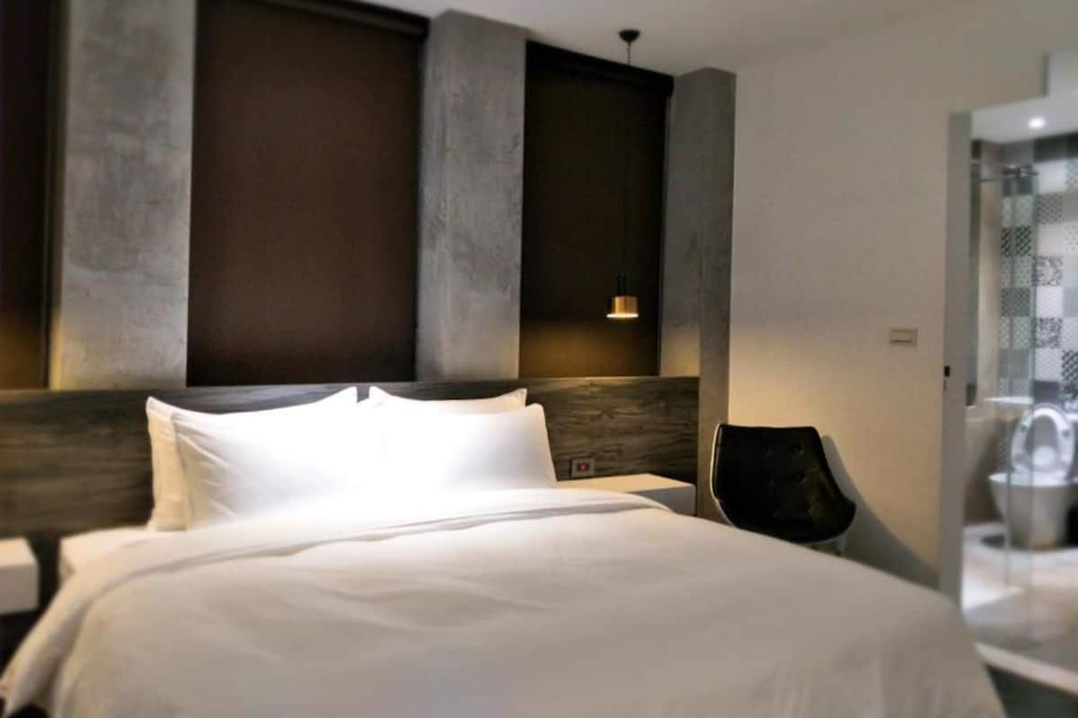 A modern hotel room with a large bed, a wooden headboard, and a nightstand.