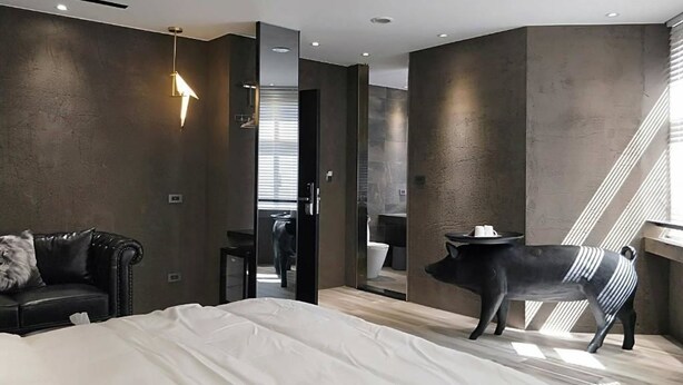 A modern bedroom with a large bed, a black leather sofa, a unique black pig sculpture, and a staircase. - Small Hotel (Luodong)