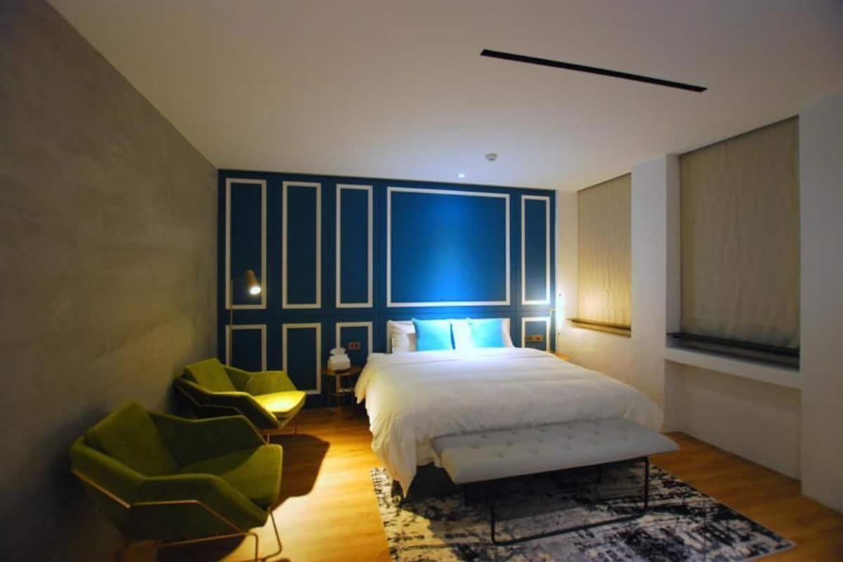A modern bedroom with a large bed, green chairs, a patterned rug, and a blue accent wall.