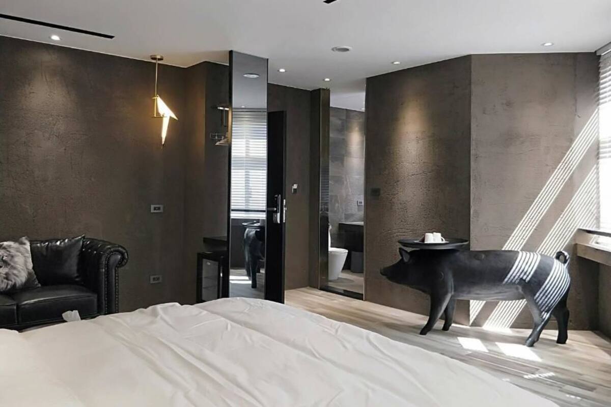 A modern bedroom with a bed, a black chair, a small table, and a unique black pig sculpture.