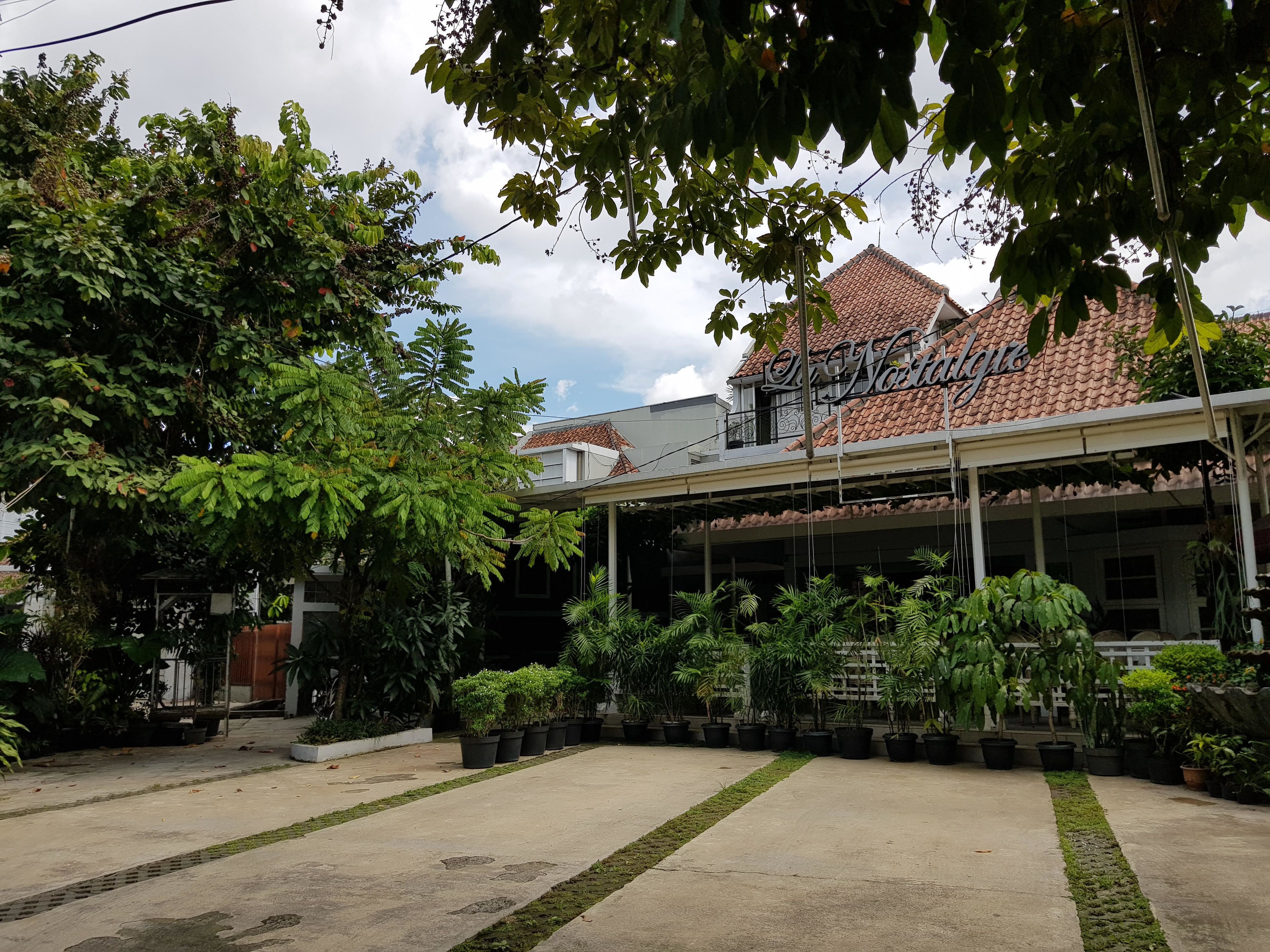 A courtyard with potted plants, a building with a tiled roof, and a sign reading "La Nostalgia".