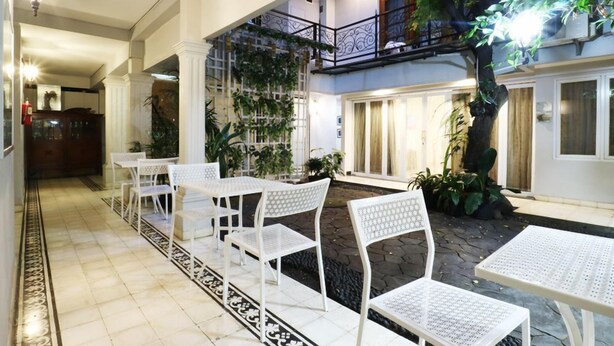 Un espace patio intérieur avec des tables et des chaises en métal blanc, entouré de plantes en pot et agrémenté d’un mur décoratif.