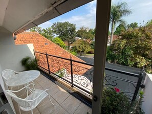 Un balcon doté d’un toit en tuiles, de chaises en métal peintes en blanc et d’une rambarde décorative en métal.