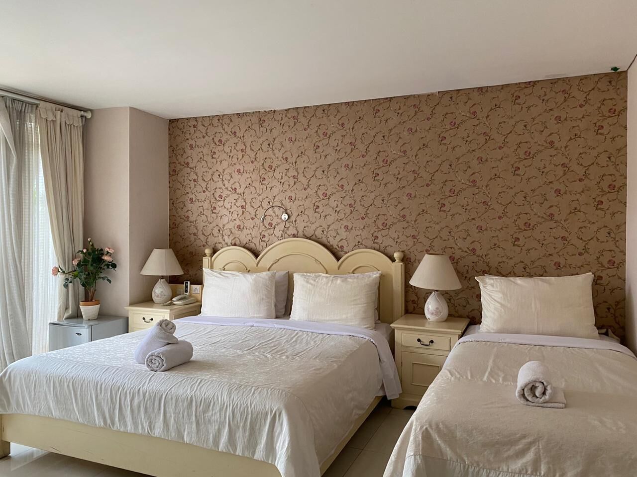 A double bed with a headboard, two bedside tables, a lamp on each table, and a floral-patterned wall.