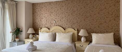 A double bed with a headboard, two bedside tables, a lamp on each table, and a floral-patterned wall.