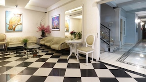 Un hall d’entrée avec un sol à carreaux, un canapé, une petite table et deux chaises. Les murs sont ornés de tableaux et un escalier mène à un autre espace.