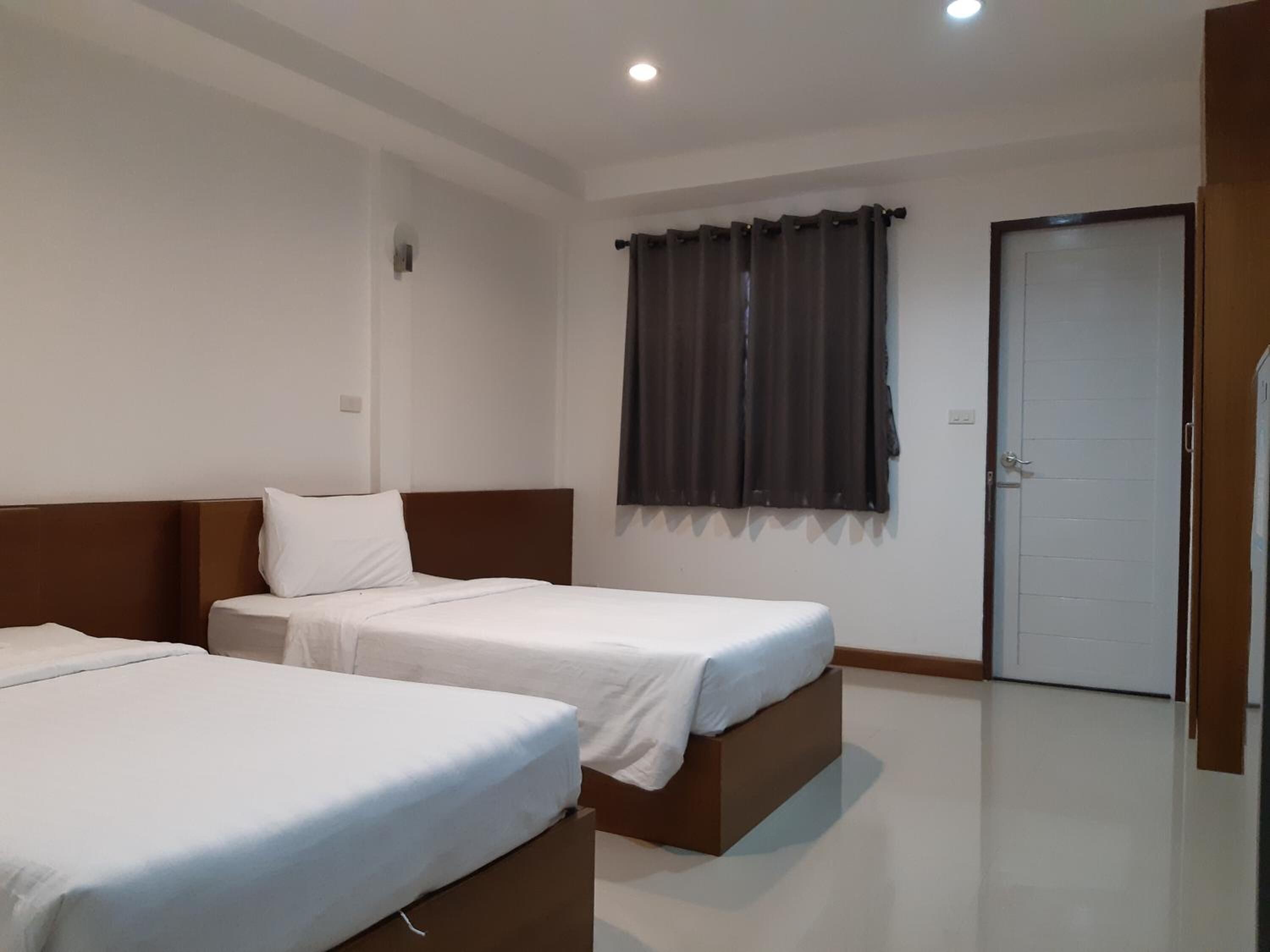 A hotel room with two single beds, a door, and a window with curtains.