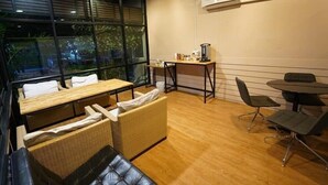 A room with a wooden table, wicker sofa, and a small kitchenette area. - The Chill House (Tha Muang)